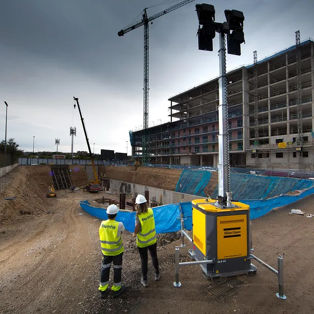 To arbeidere står vevd lystårn på anleggsområde